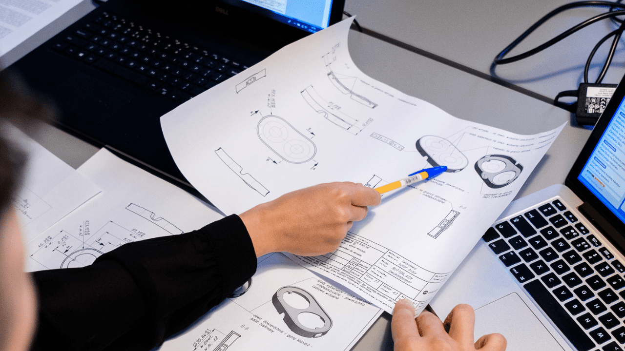 Team of people discussing engineering designs on paper and digitally.